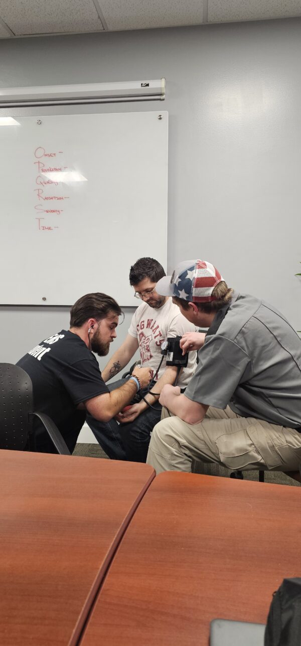 An EMT instructor inside an ambulance demonstrates proper technique on an infant manikin for a group of young children, providing a public outreach learning experience.